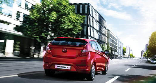 Rear view of red Accent5DR driving fast through the building in the city