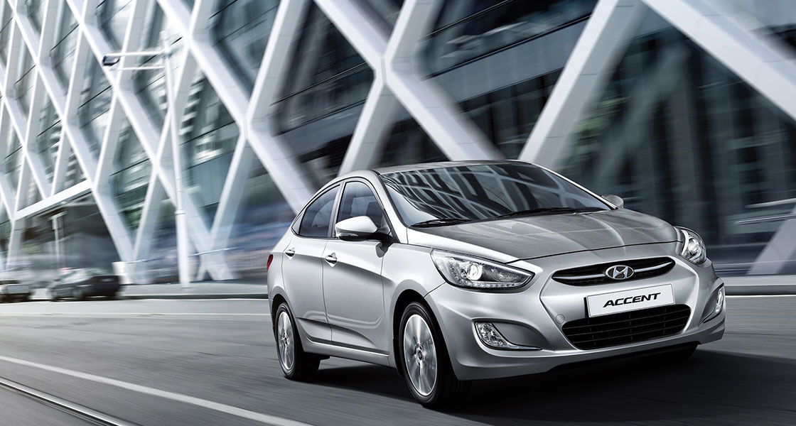 Side-front view of silver Accent passing by cross patterned wall building