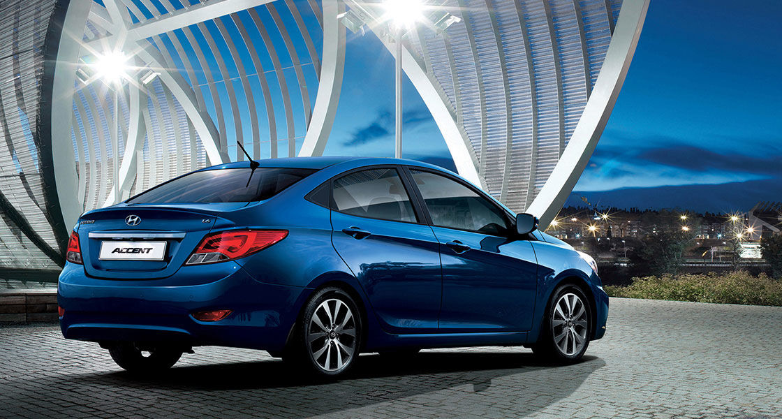 Side-rear view of blue Accent parked in front of the arch shaped architecture in the evening