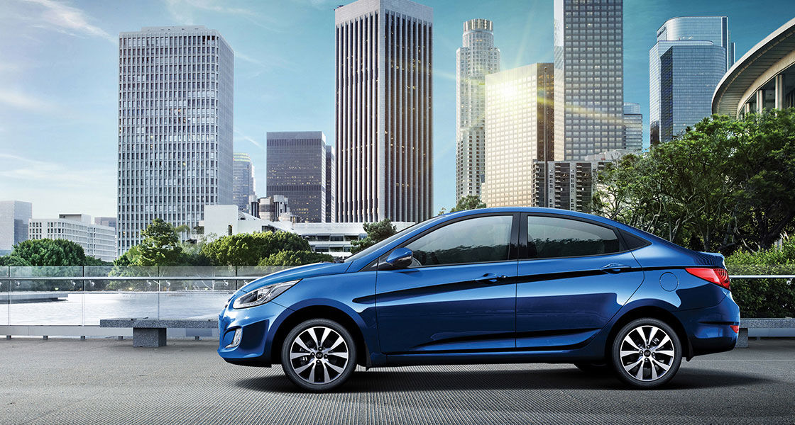 Side view of blue Accent driving on the road with city sky view behind