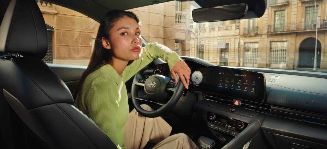 Image of a woman wearing a green cardigan leaning her arm on the steering wheel of the new Elantra