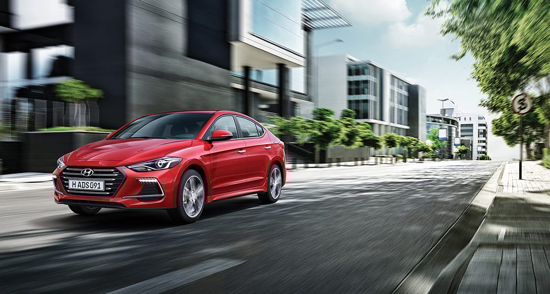 Left side front view of red Elantra Sport driving on the street