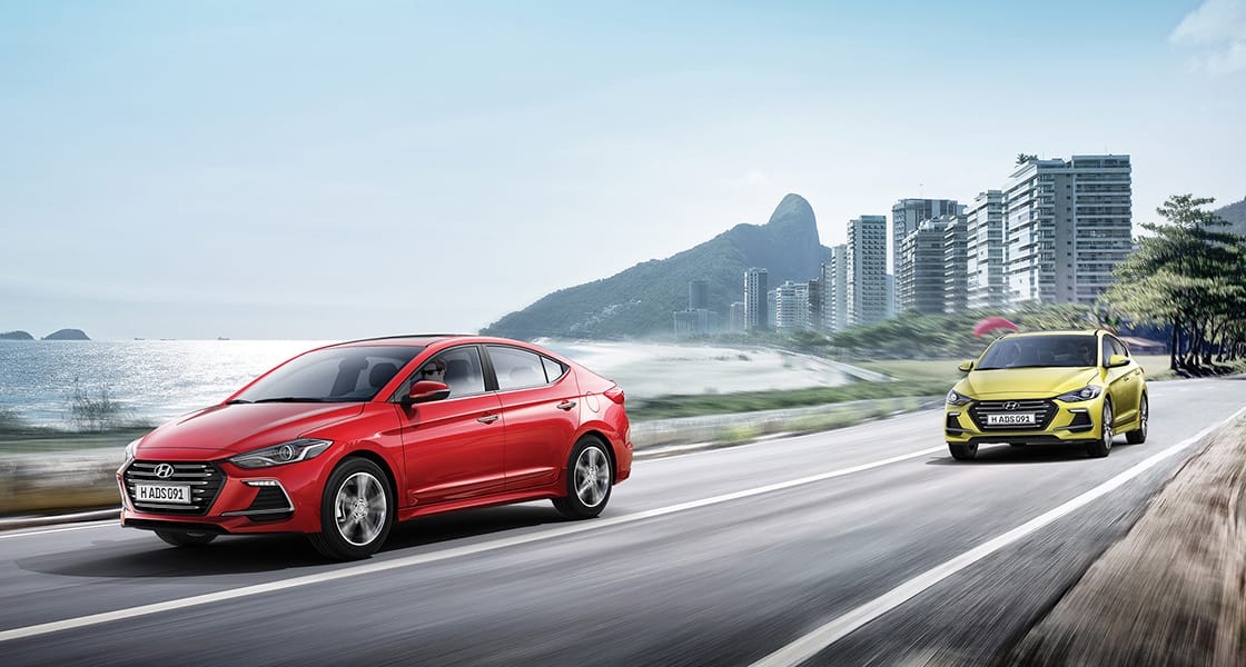 Left side front view of two Elantra Sport cars driving on the road with the city background