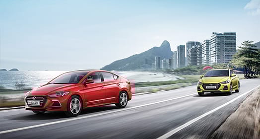 Left side front view of two Elantra Sport cars driving on the road with the city background