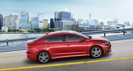 Side view of red Elantra Sport on the road with buildings background