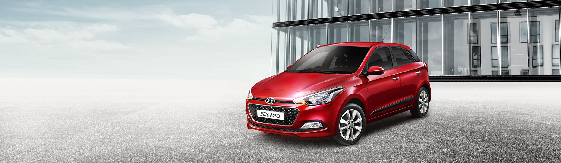 Red color Elite i20 is placed in front of a modern building