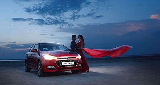 A couple standing next to red Elite i20 headlight on the beach in the evening