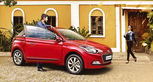 A man getting to the passenger's seat of red Elite i20 parked in front of yellow building