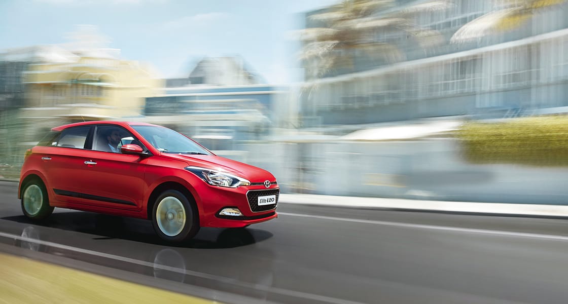 Side view of red Elite i20 driving fast on the road in the city