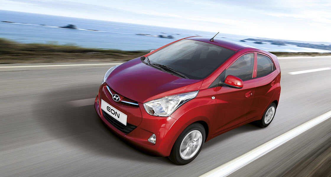 Left side front view of red Eon driving on the road with the beach beside