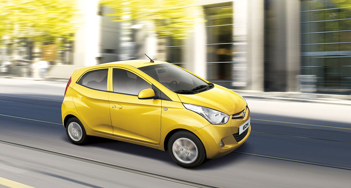 Right side-front view of yellow EON passing by the building