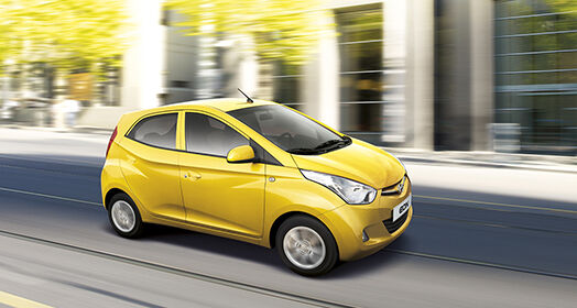 Right side-front view of yellow EON passing by the building