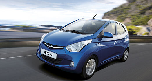 Side-front view of blue Eon passing by coastal road