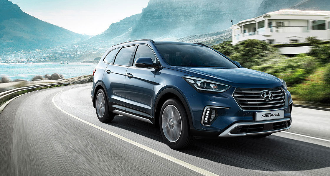 Side front view of navy Grand Santafe driving fast on the mountain side road