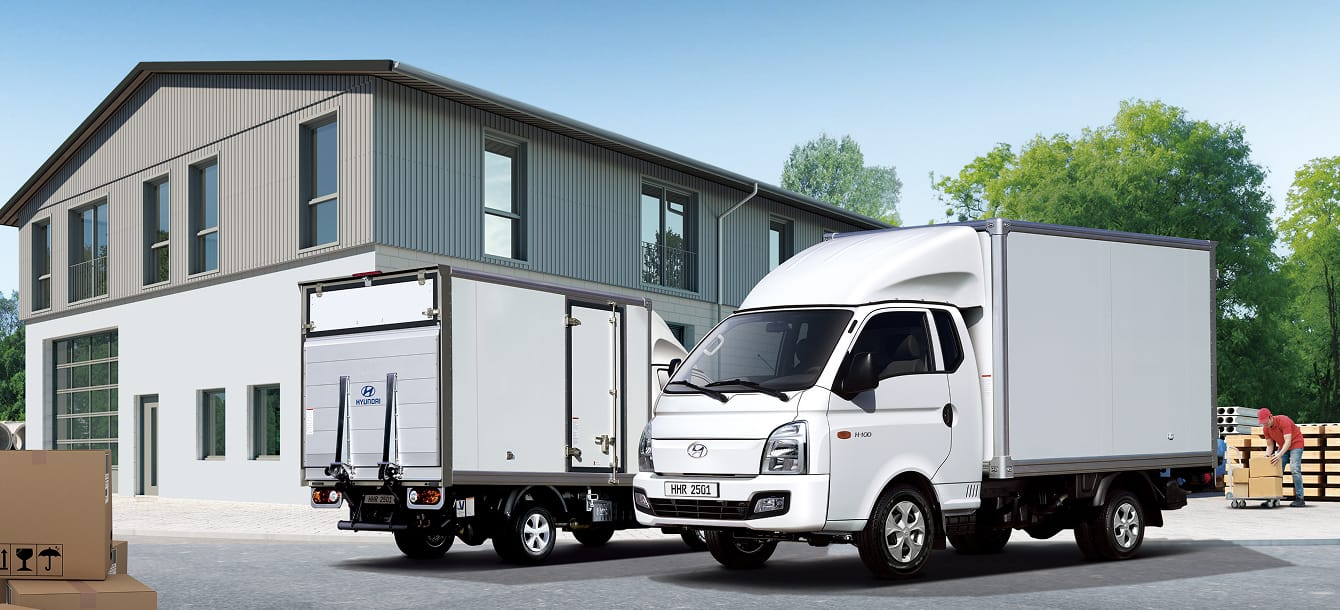 A built-in model vehicle parked in front of a logistics warehouse, with a person organizing goods to be loaded behind the vehicle.