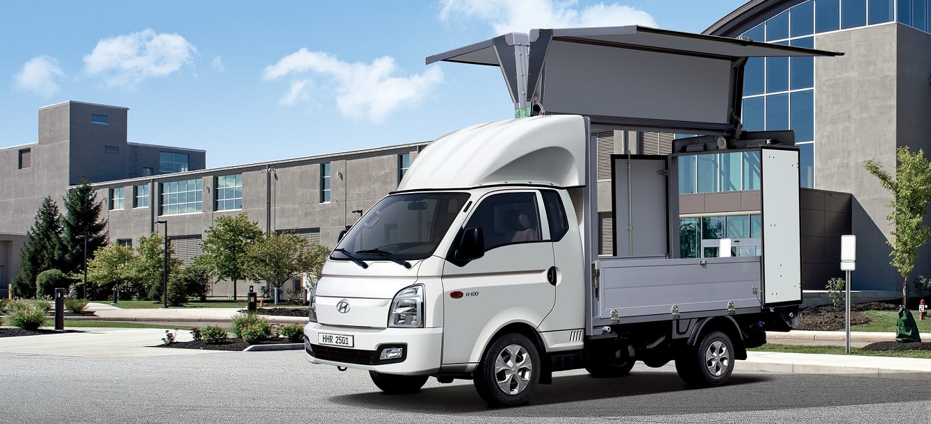 A wing body vehicle parked in front of a building with both wings and the rear door open.