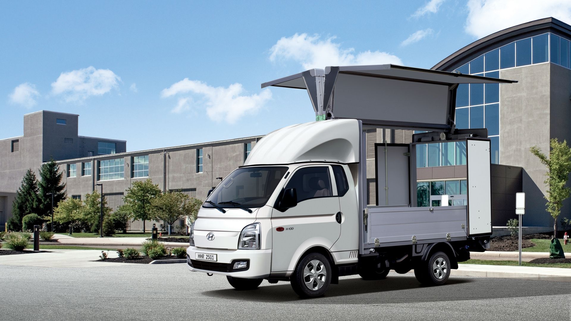 A wing body vehicle parked in front of a building with both wings and the rear door open.