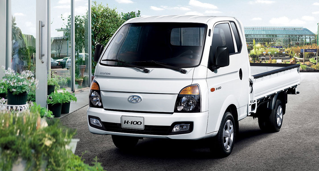 Side-front view of white H-100 parked in front of plant market