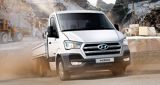 Side front view of white H350 driving roughly on the road