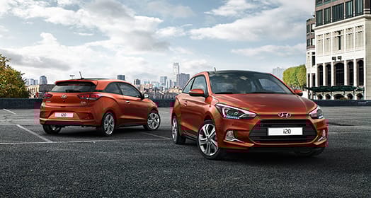 Front side view of i20 coupe in front and side-rear view of tangerine orange i20 coupe parked behind with skyline view