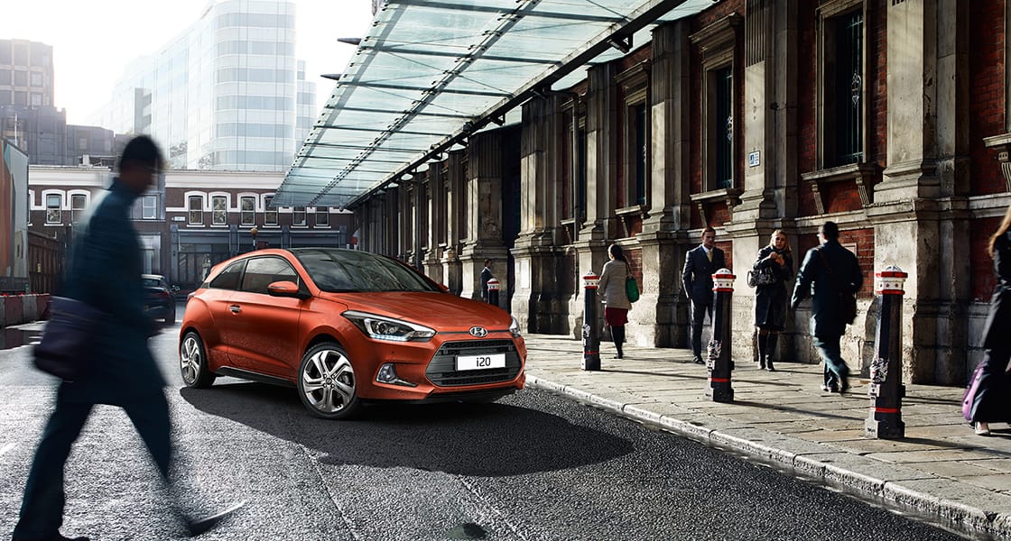Side front view of tangerine orange i20 parked next to pedestrians road