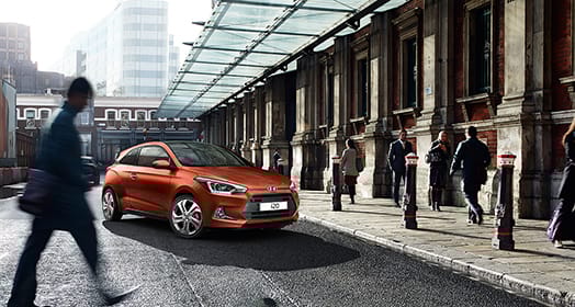 Side front view of tangerine orange i20 parked next to pedestrians road