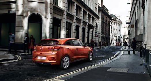 Side-rear view of tangerine orange i20 driving by buildings