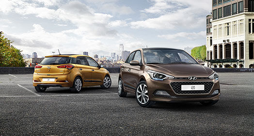 Front side view of brown i20 in front and side-rear view of mandarin orange i20 parked behind with skyline view
