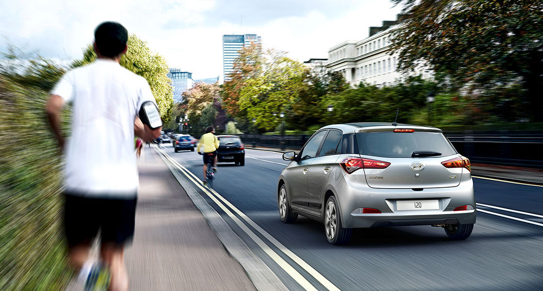 Side-rear view of silver i20 driving next to running man on a clear day