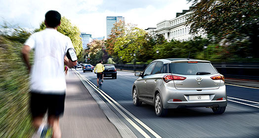 Side-rear view of silver i20 driving next to running man on a clear day