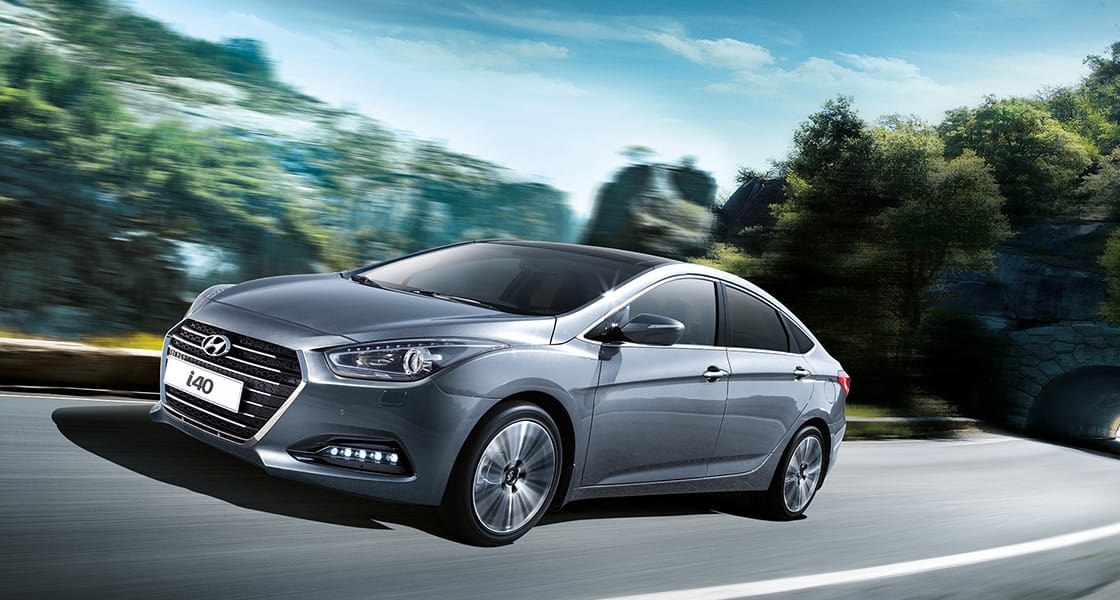 Side front view of dark gray i40 sedan driving on the mountainous road