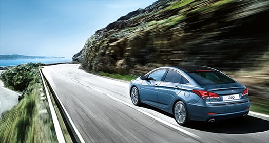 Side rear view of navy i40 sedan driving fast on the mountainous road on a clear day