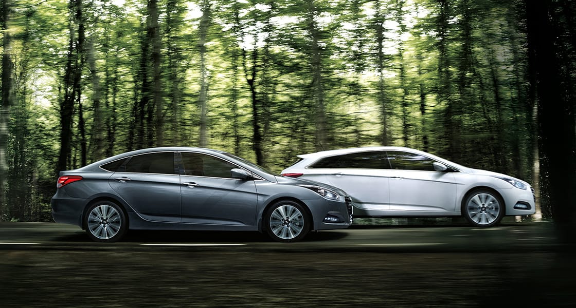 Side view of white and dark gray i40 sedans driving in the forest