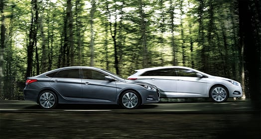 Side view of white and dark gray i40 sedans driving in the forest