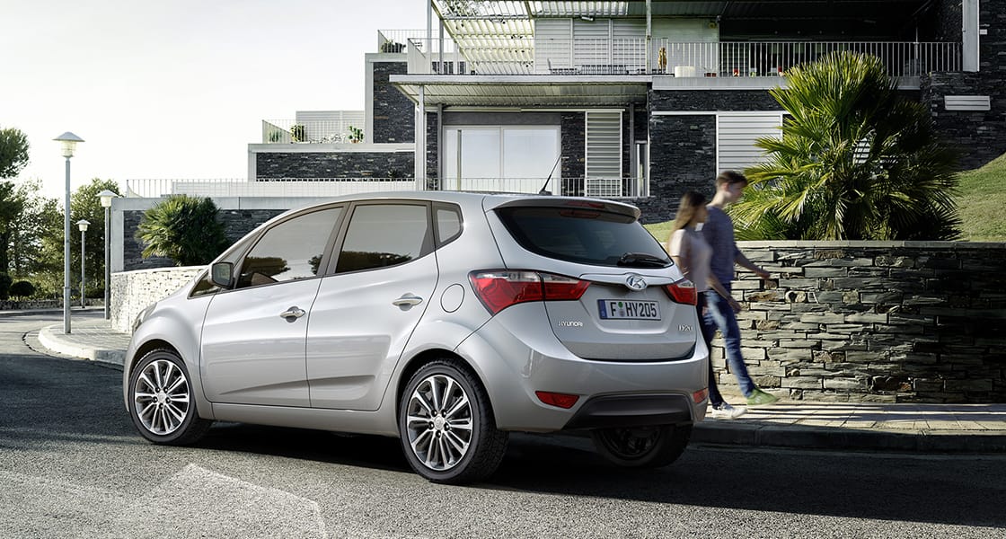 Side rear view of light gray ix20 passing through the residential street