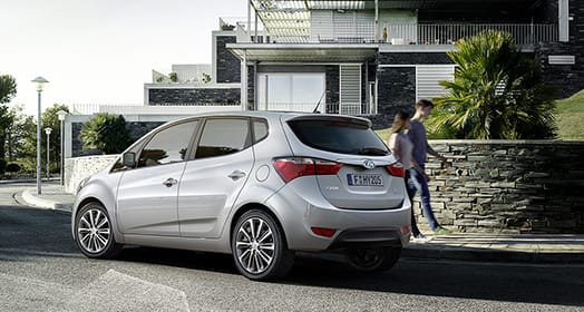 Side rear view of light gray ix20 passing through the residential street