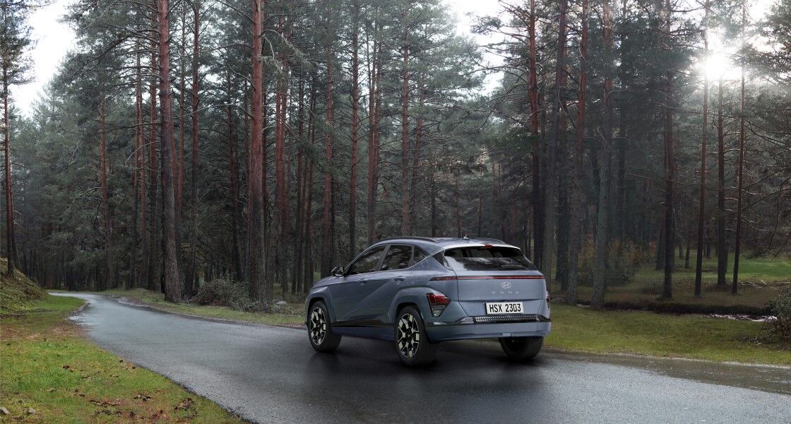 The rearview of a blue The all-new KONA driving on a road in the forest