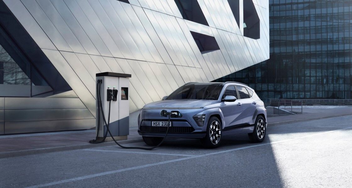 A blue The all-new KONA Electric is charging at an electric vehicle charging station.