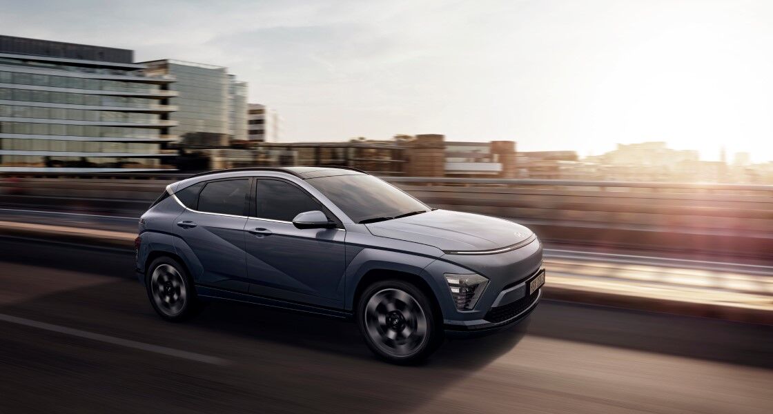 Right side view of a blue The all-new KONA speeding over a bridge