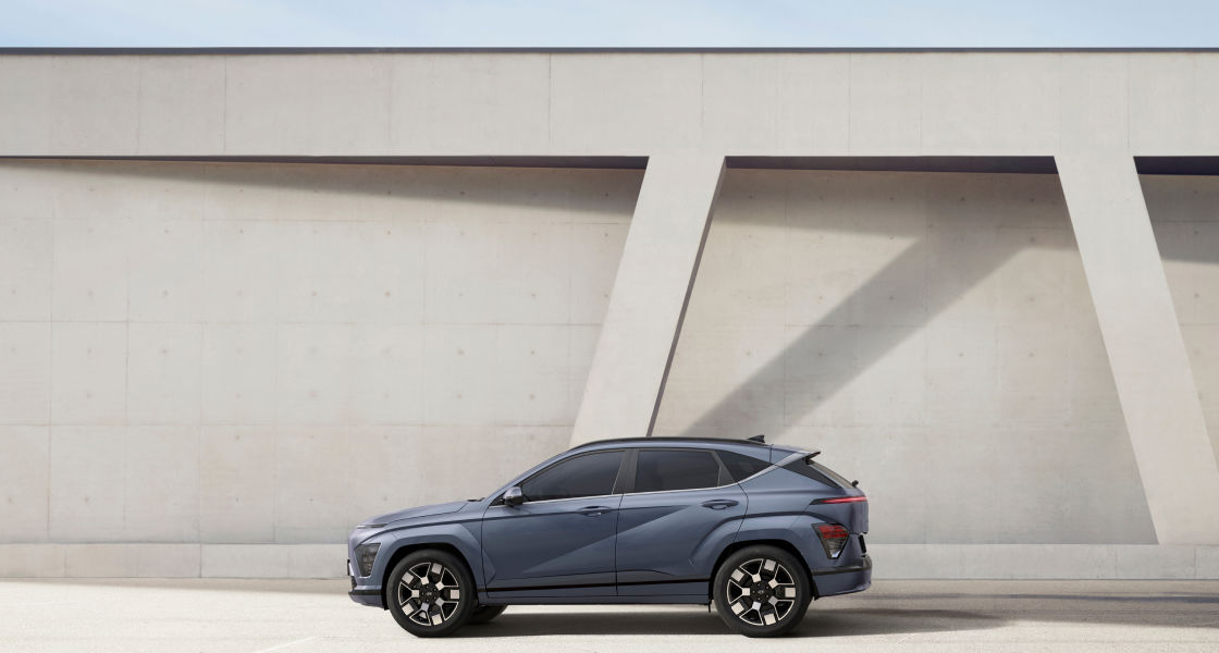 السيارة كونا الجديدة كليًا ذات اللون الأزرق تقف أمام جدار أبيض وجانبها الأيسر مواجه للأعلى.