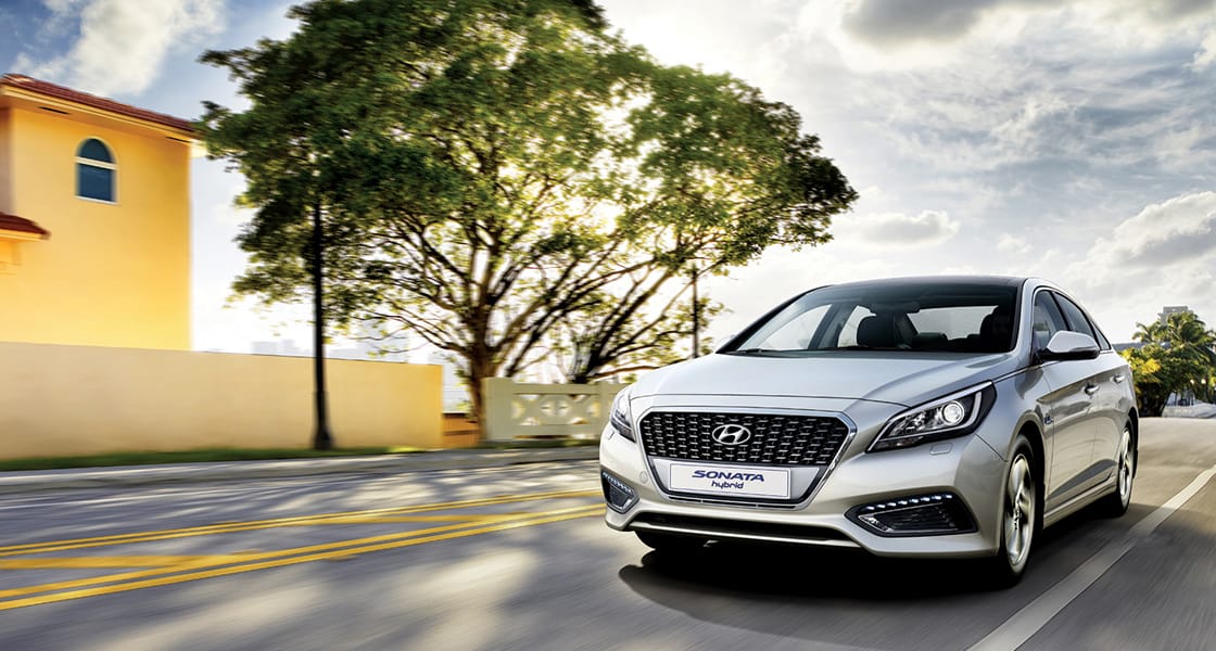 Left side front view of silver Sonata hybrid driving on the road