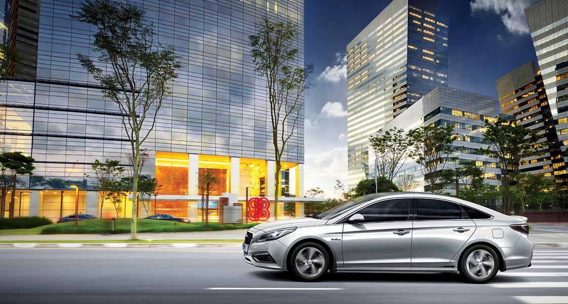 Side view of driving silver Sonata hybrid passing by buildings