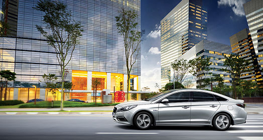 Side view of driving silver Sonata hybrid passing by buildings
