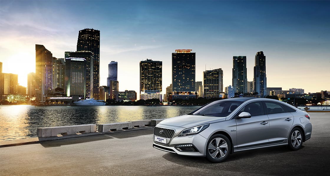 Side front view of gray Sonata Hybrid parked lakeshore in the evening with skyline background