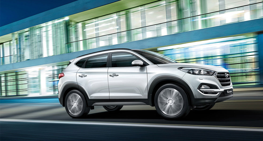 Side view of driving silver Tucson passing by the one-story building