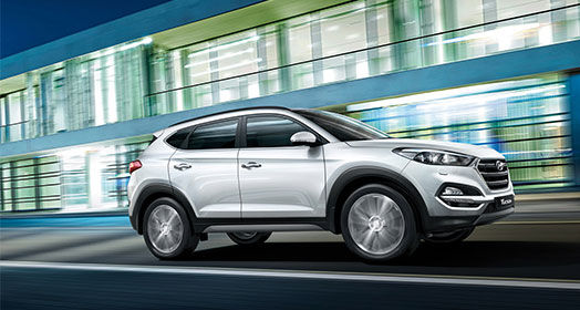 Side view of driving silver Tucson passing by the one-story building