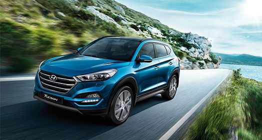 Left side front view of light blue Tucson driving on the mountainous road