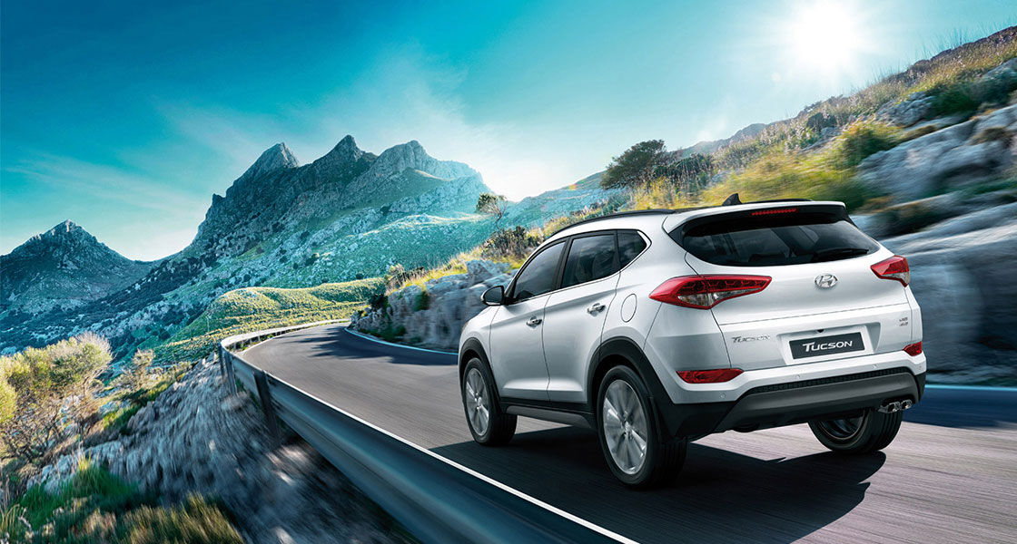 Left side rear view of light silver Tucson driving on the mountainous road