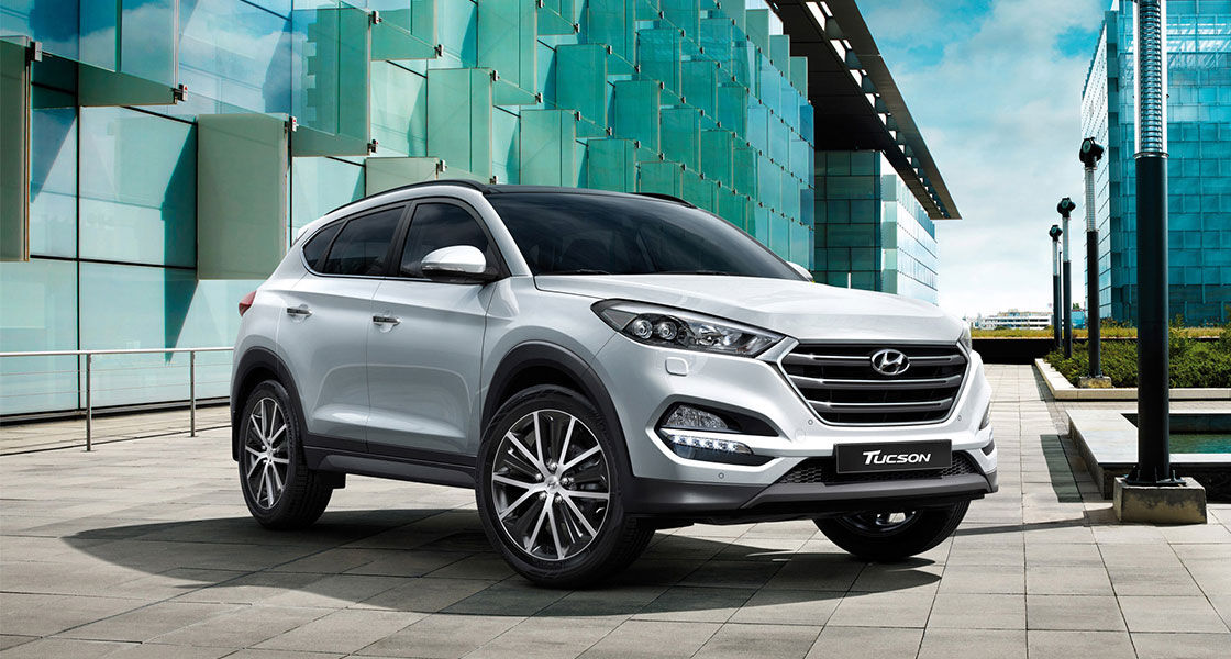 Right side front view of light silver Tucson on the street with the building behind