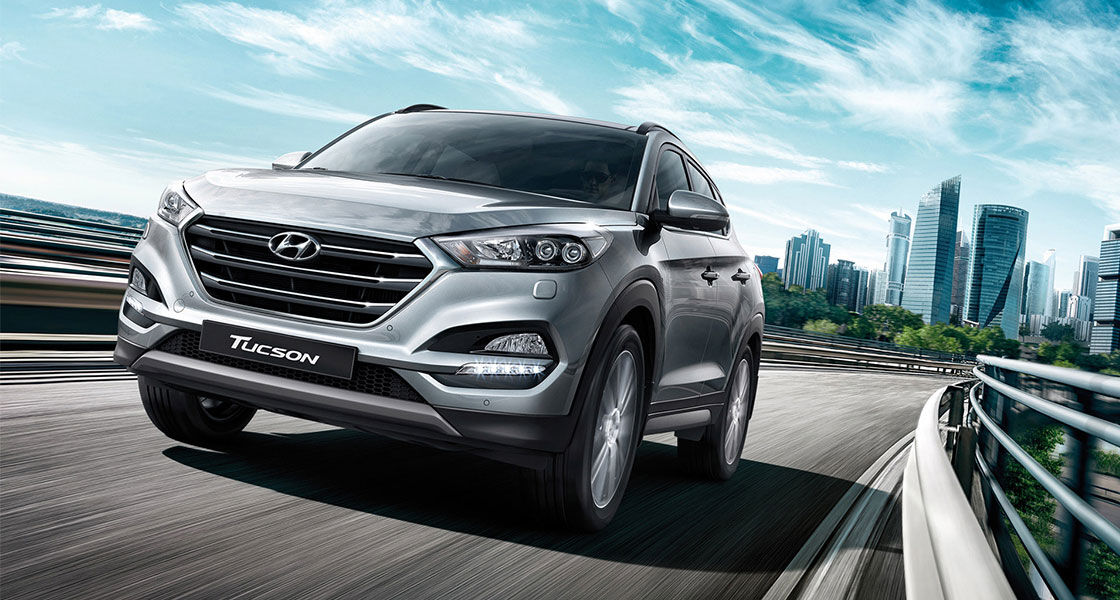 Front view of silver Tucson driving on the road with the city background